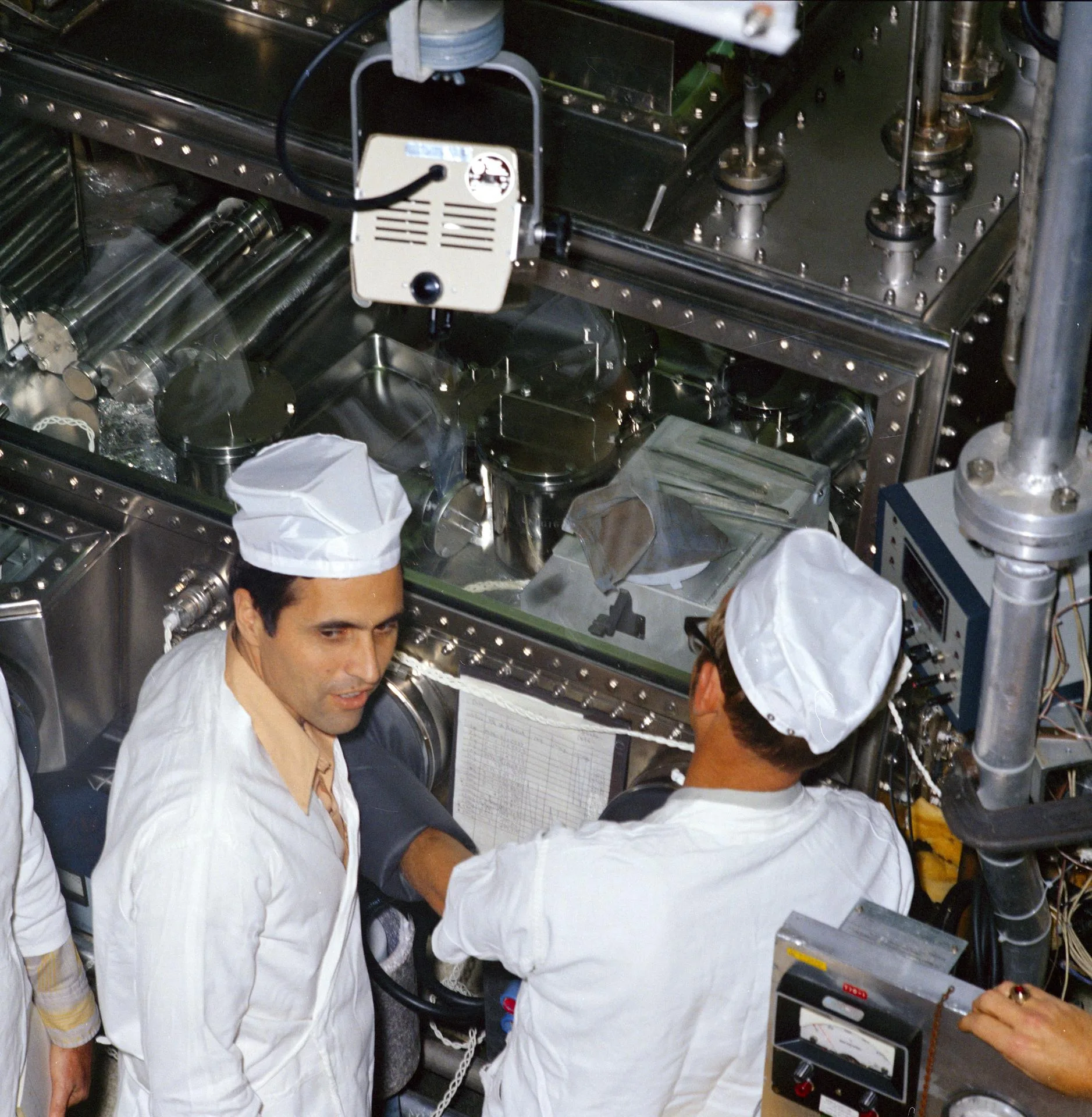 Two technicians in white clean-room caps work at a sealed sample-handling glove box at NASA's Lunar Receiving Laboratory