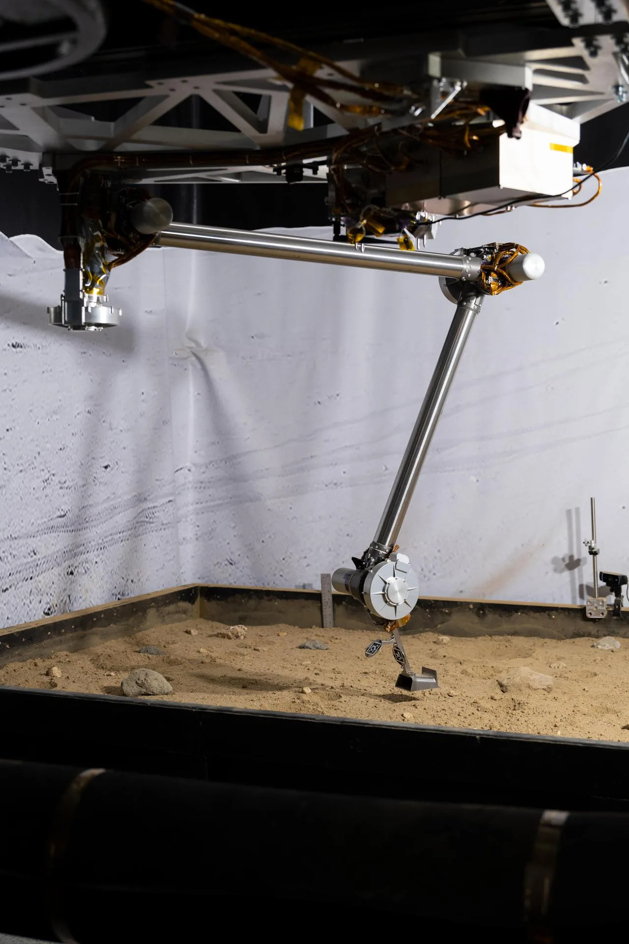 NASA's COLDArm robotic arm with a 3D-printed titanium scoop poised above a lunar regolith simulant test bed in the laboratory