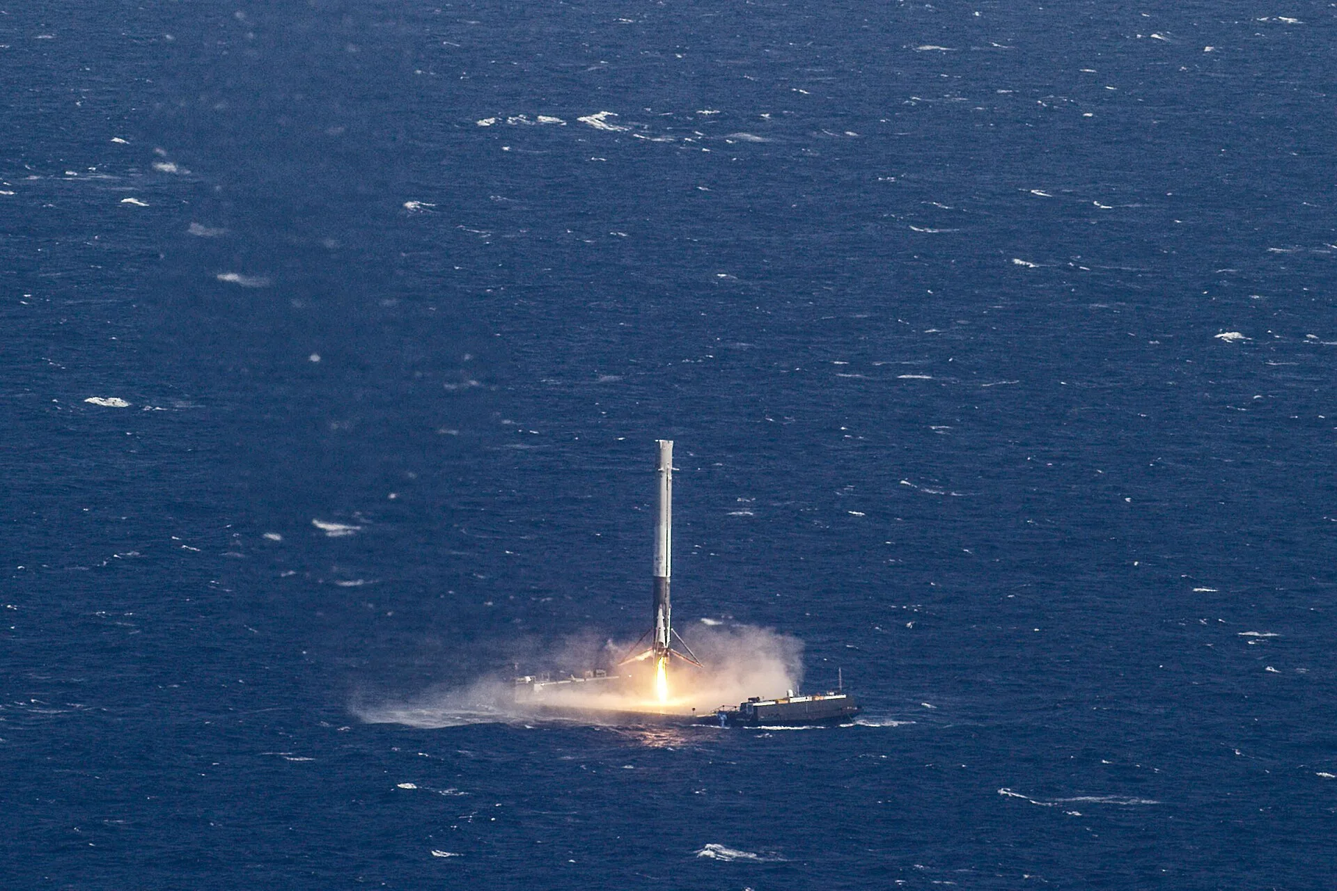 A Falcon 9 first stage standing upright on a droneship at sea, its landing engine still firing