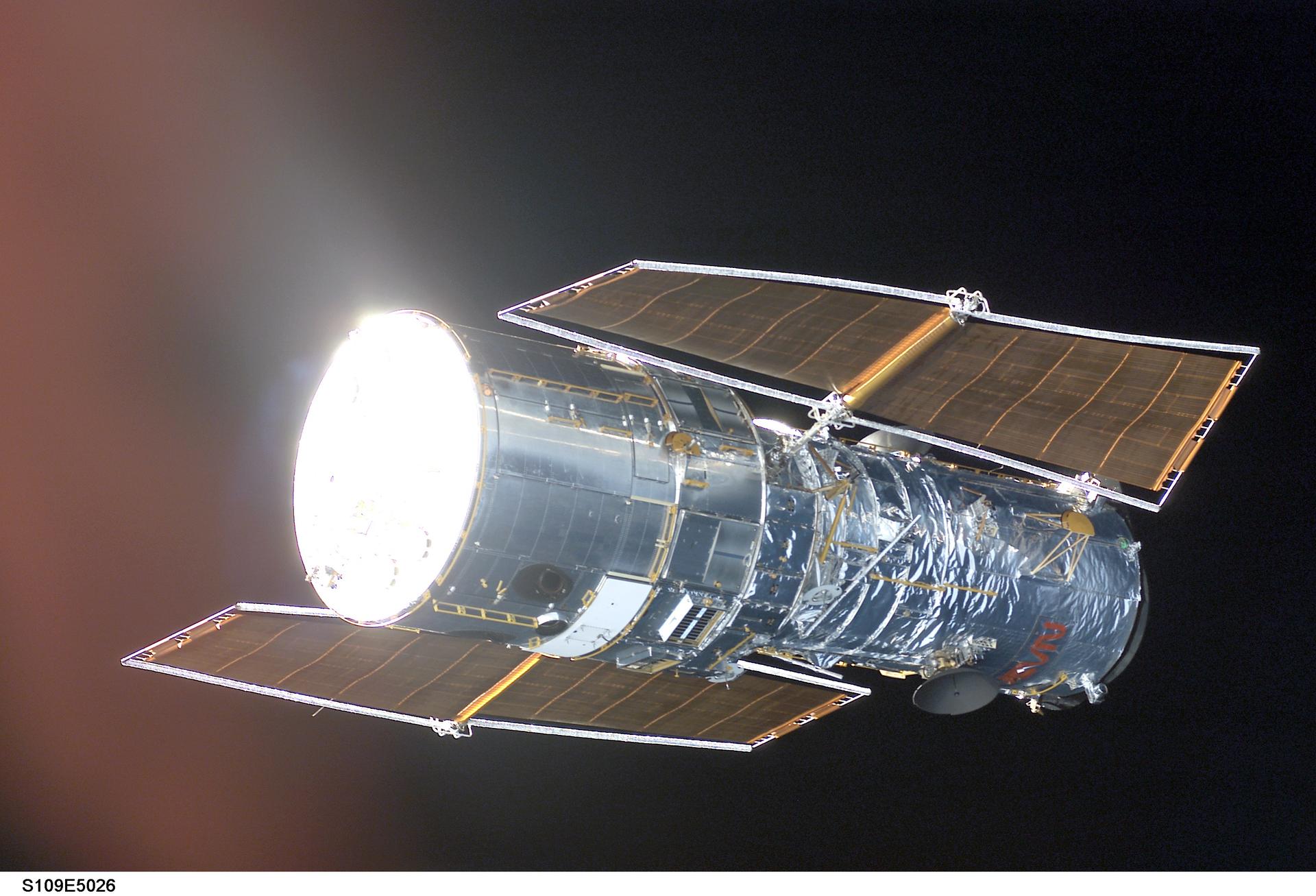 The Hubble Space Telescope photographed from Space Shuttle Columbia during the fourth servicing mission STS-109 in March 2002, showing its cylindrical body, gold thermal insulation, and deployed solar arrays against black space with the blue Earth limb visible below
