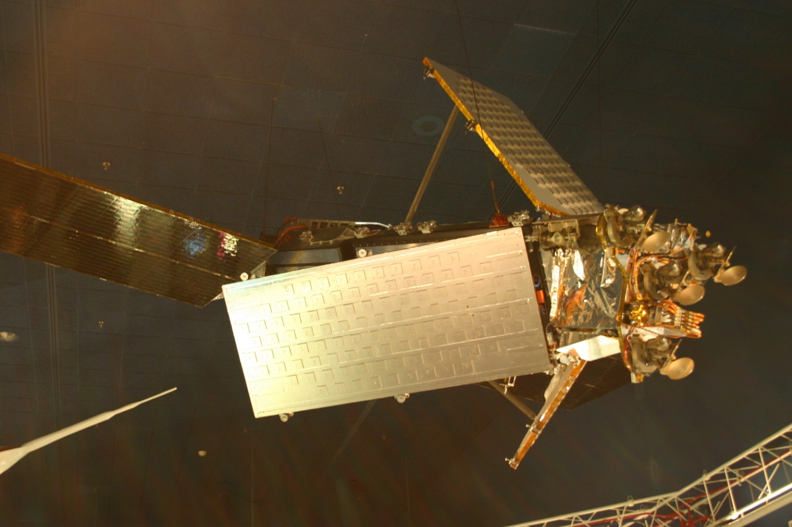 An Iridium communications satellite with gold-foil solar wings and a flat phased-array antenna panel, displayed against a dark backdrop