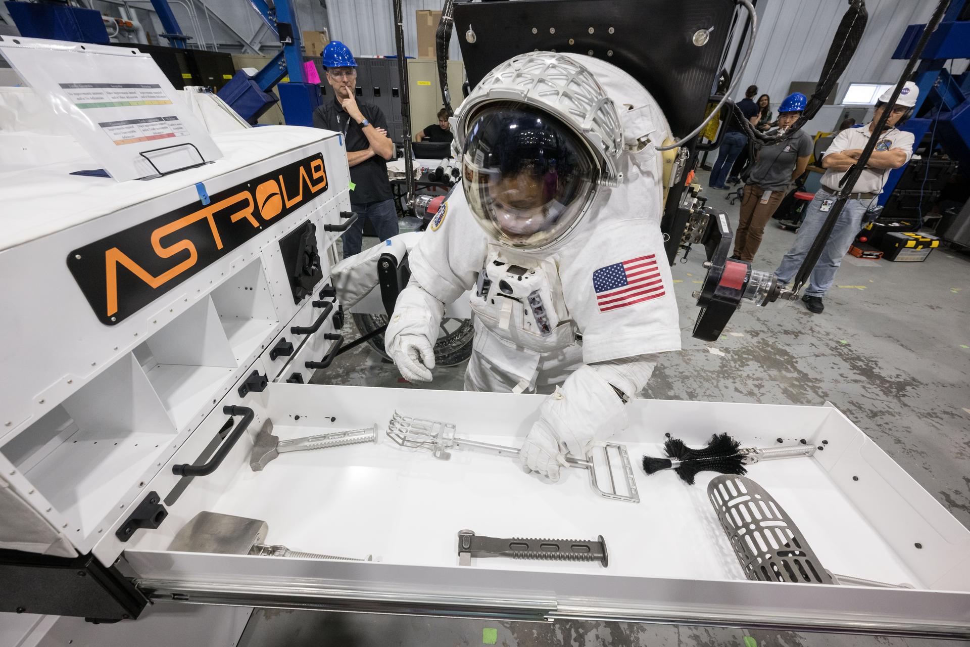 A NASA astronaut in a pressurised test suit reaches into an open tool drawer on Astrolab's FLEX lunar terrain vehicle during a Johnson Space Center evaluation
