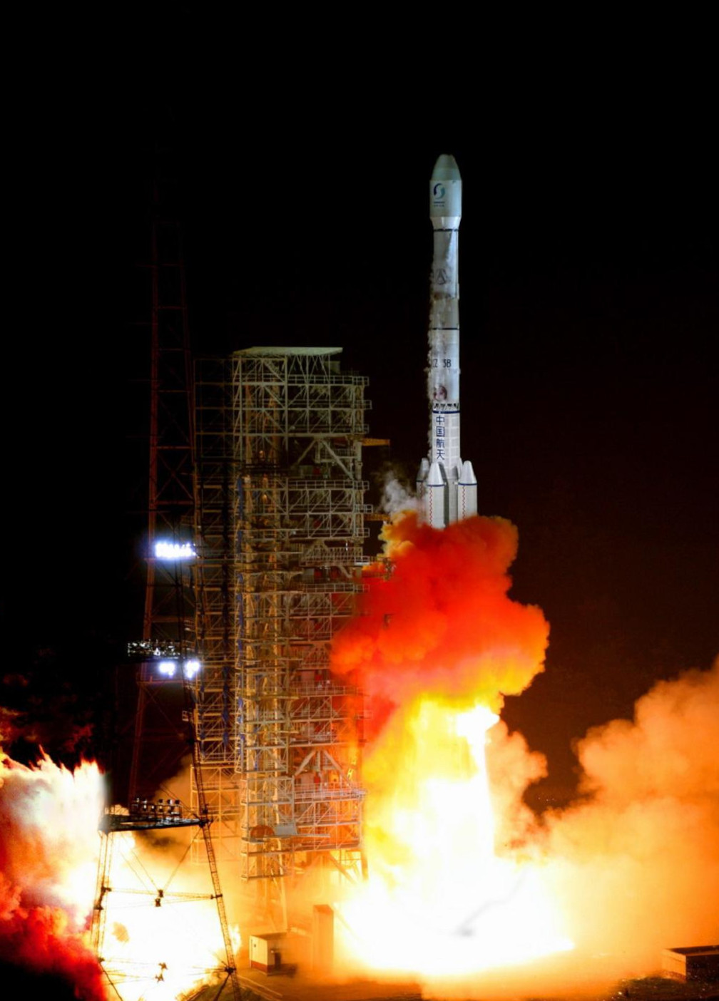 A Long March 3B rocket lifting off at night from a launch tower amid bright orange exhaust flames