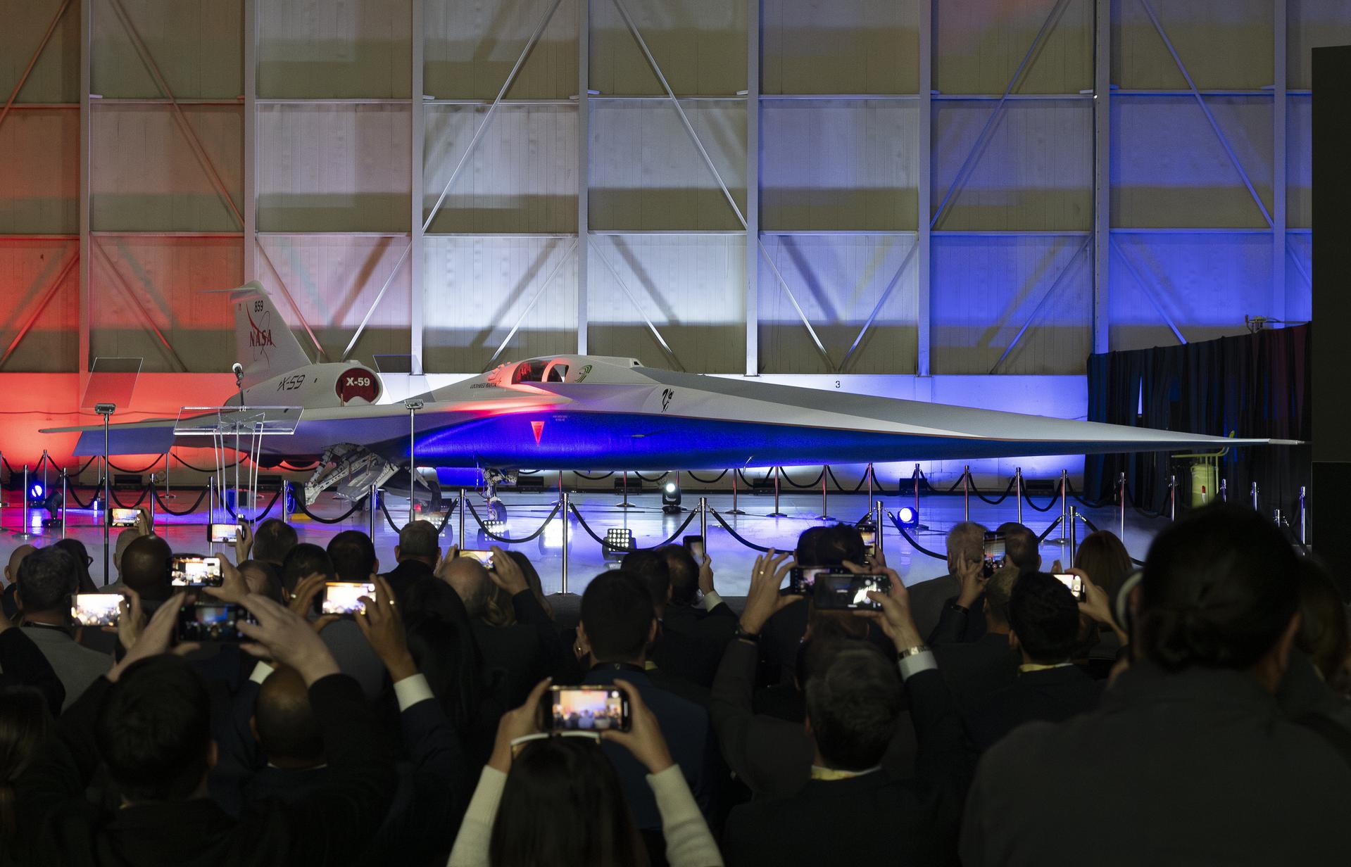 NASA's X-59 quiet supersonic research aircraft unveiled at Lockheed Martin Skunk Works in Palmdale, California on January 12, 2024, lit by red, white, and blue lights as a crowd photographs it
