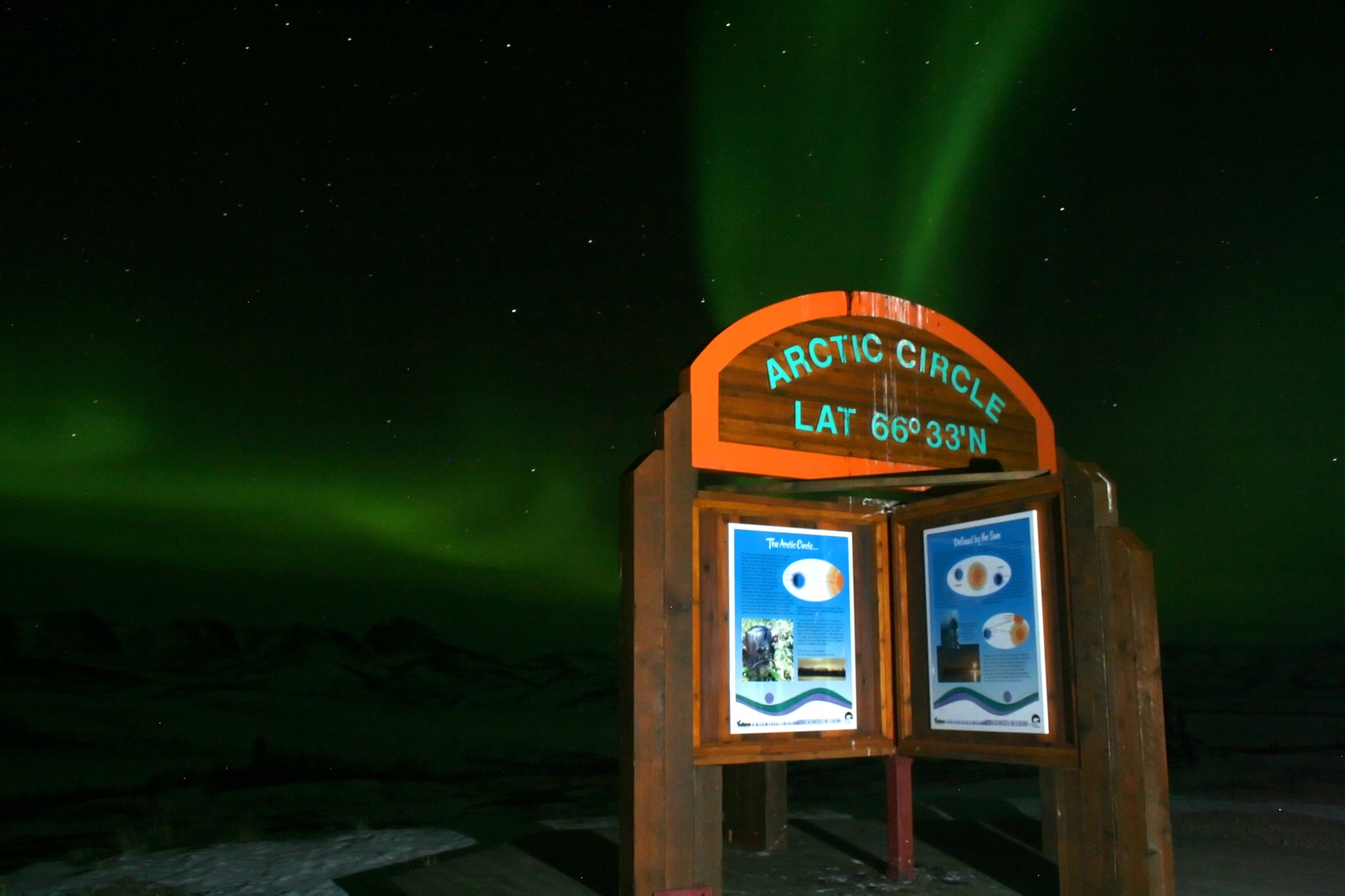 Green aurora over the Arctic Circle sign in snowy Yukon, Canada