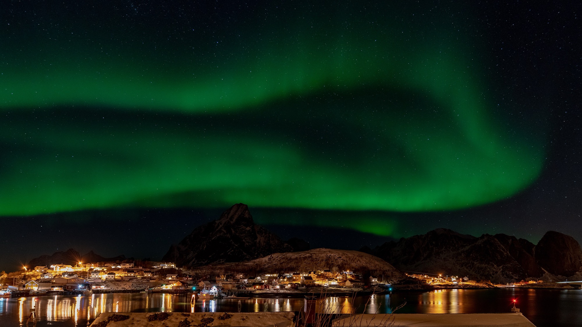Green aurora over Reine village with mountain and fjord reflections, Lofoten, Norway