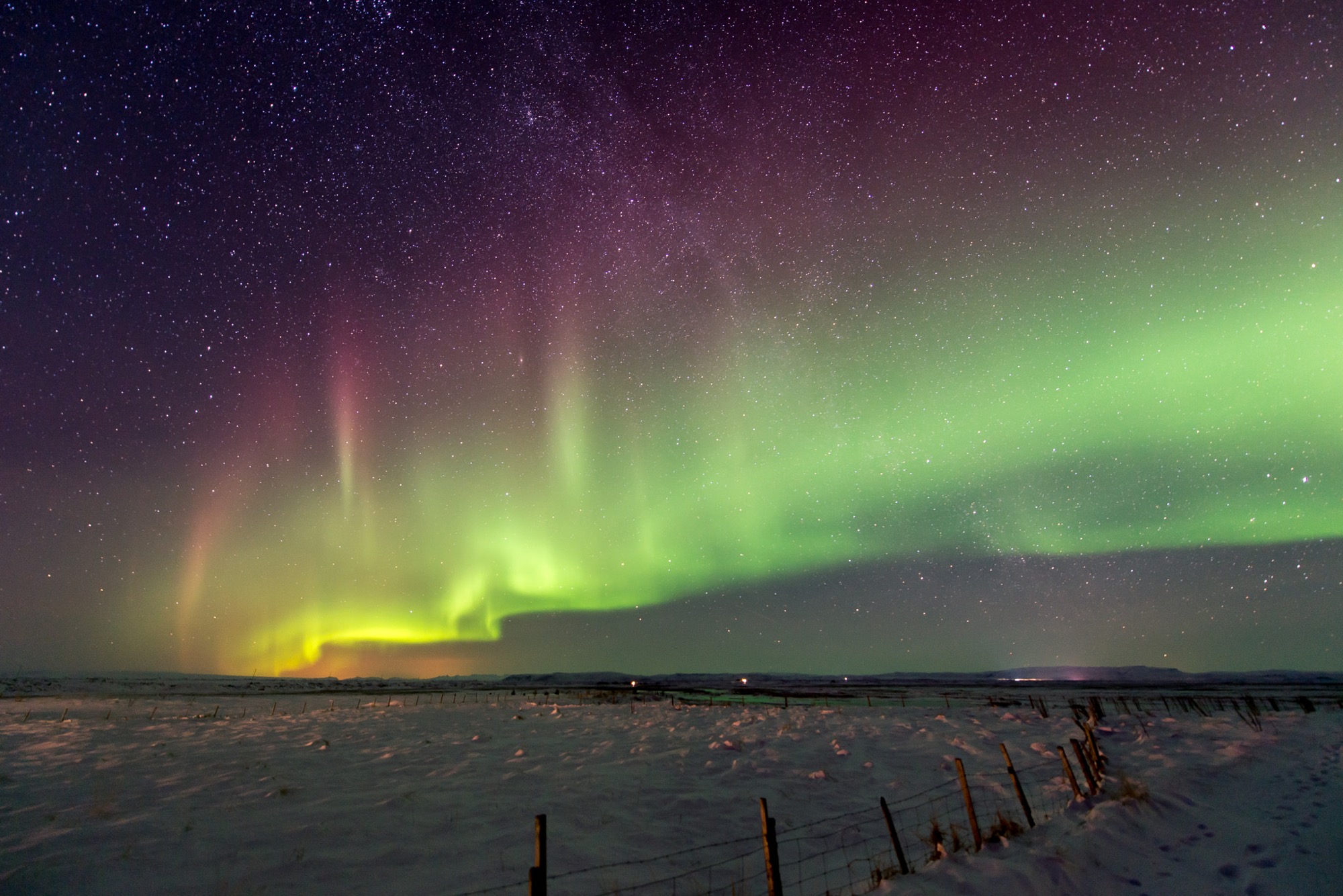 Green, red and purple aurora over a snowy field with a fence, south Iceland