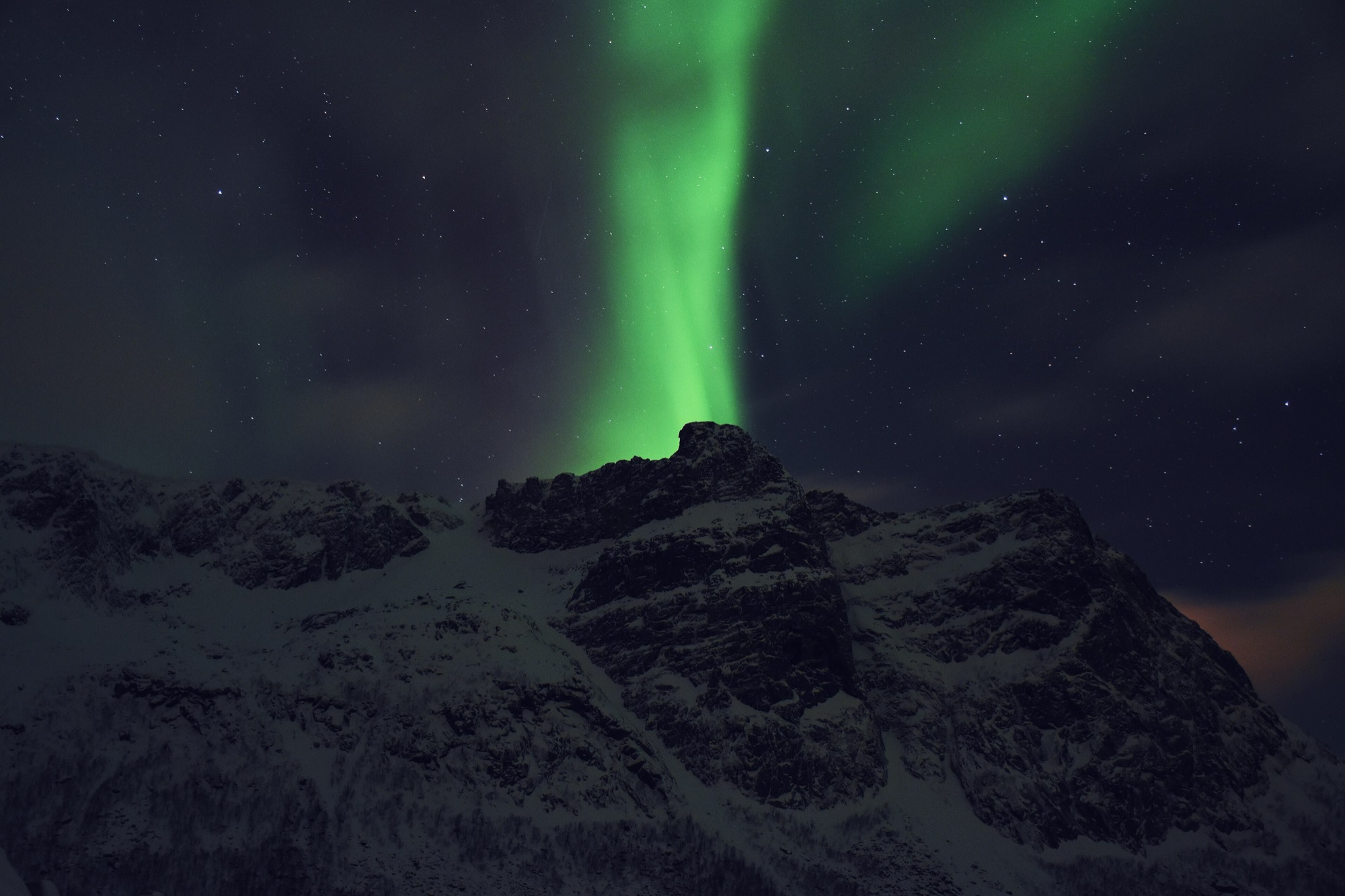Green aurora rising behind a snowy Arctic mountain peak near Tromsø, Norway