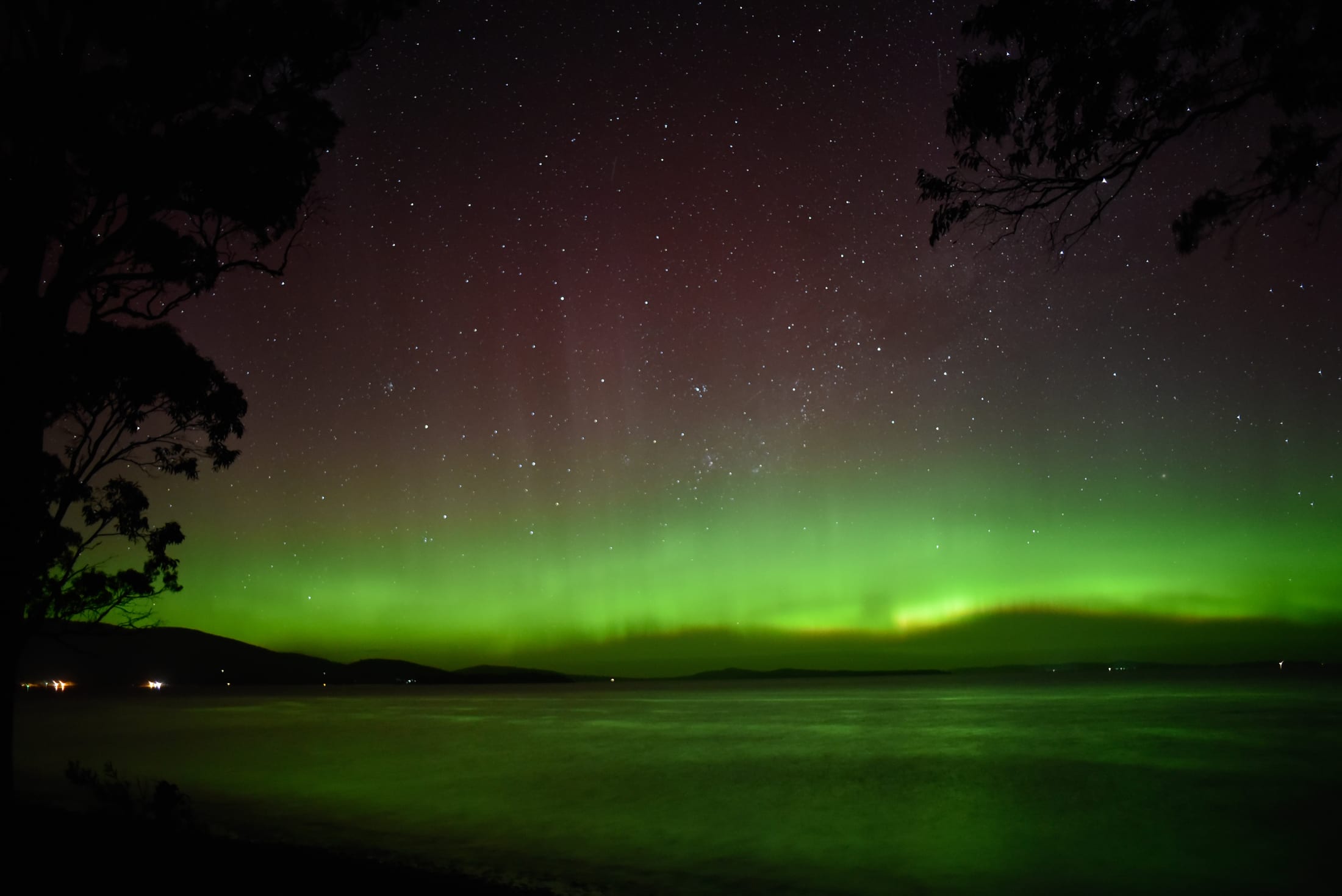 Red and green southern lights over a dark rural horizon in southern Tasmania