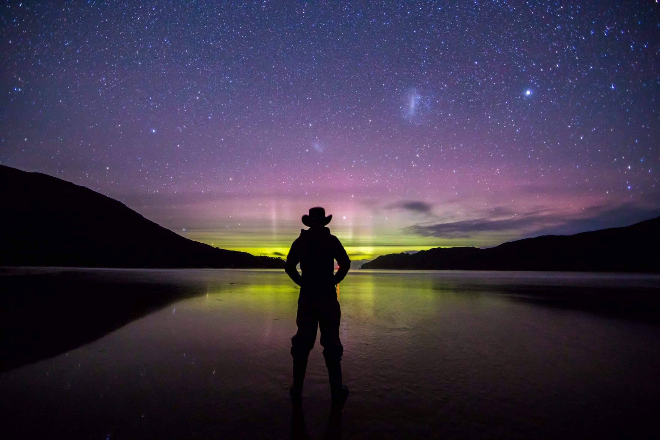 Green aurora australis over the sea with a person silhouetted on a Tasmanian beach at night
