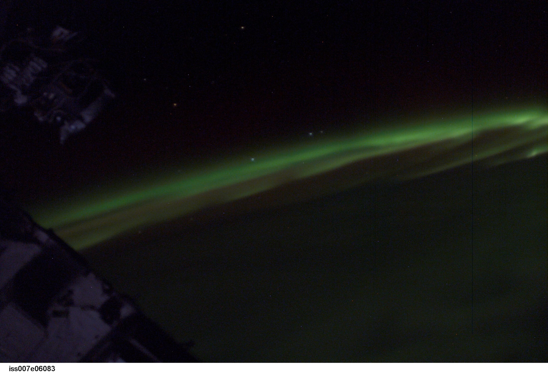 Green aurora australis band over Earth's dark limb with stars above, seen from orbit