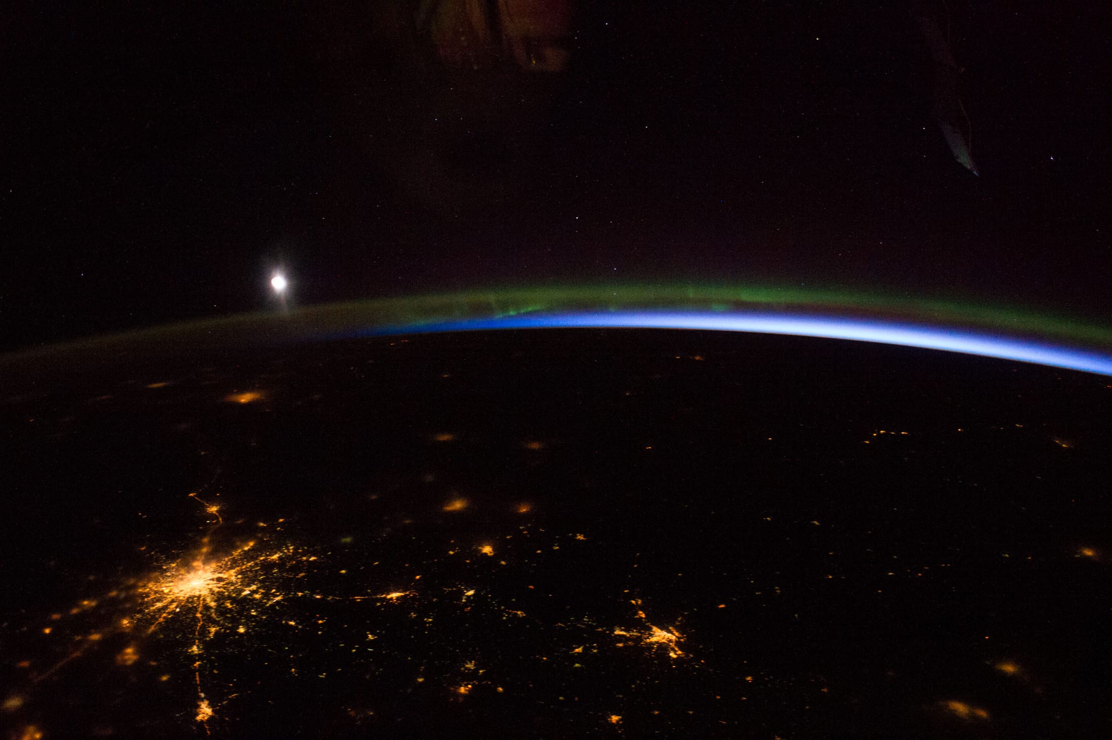 Thin green aurora and blue airglow on Earth's limb with the Moon and city lights, from orbit