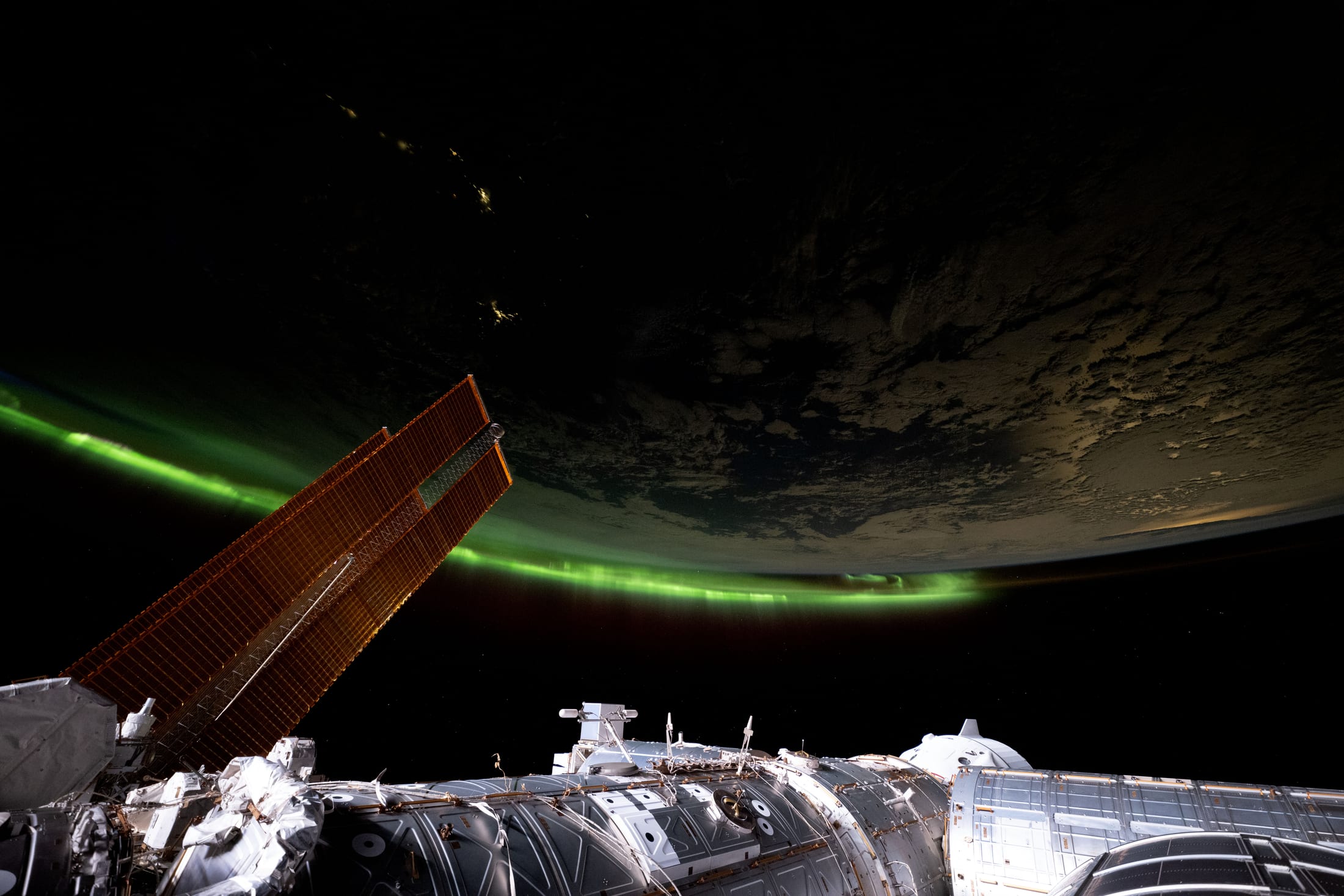 Green aurora glowing along Earth's curved horizon from orbit, an ISS solar array in the foreground