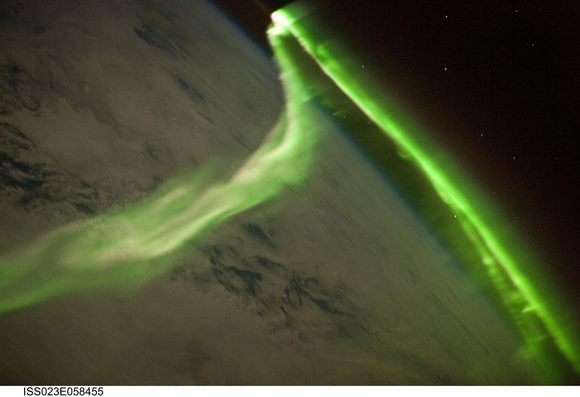 A bright green ribbon of aurora curving over Earth's dark limb seen from orbit, stars beyond