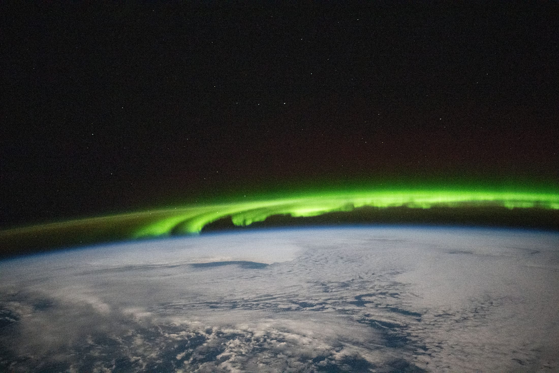 Bright green double ribbon of aurora over cloud-covered ocean, seen from orbit