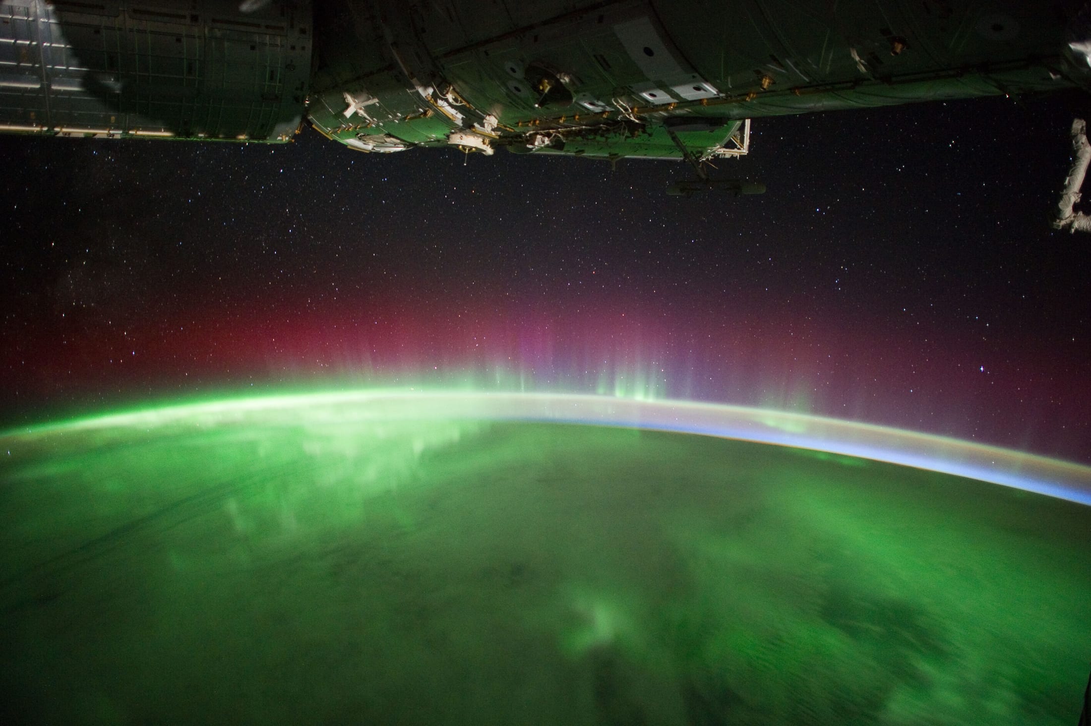 Vivid green and red aurora curtain off Earth's limb beneath ISS structure, from orbit