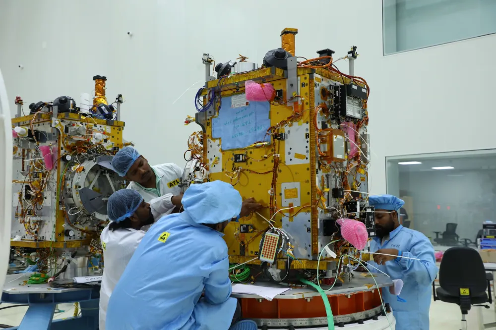 Ananth Technologies technicians in cleanroom bunny-suits performing hands-on assembly of a multi-layer-insulation-wrapped satellite.