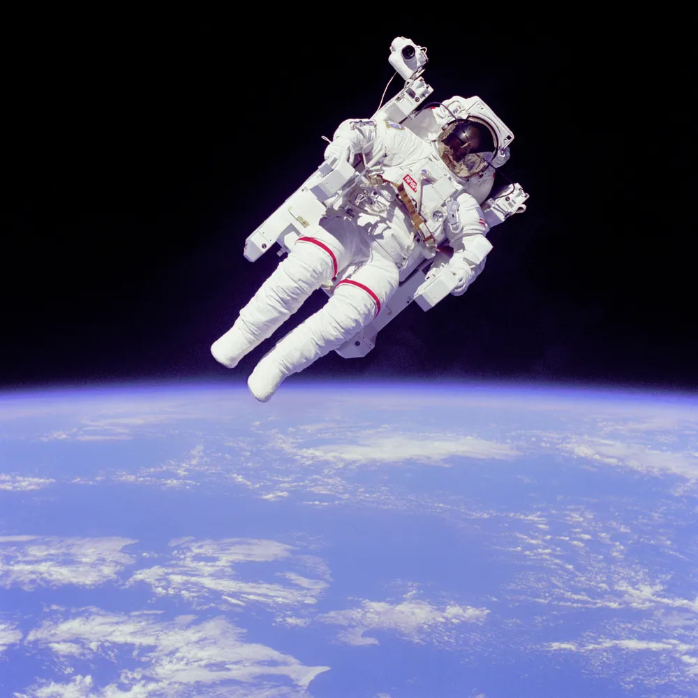 Astronaut Bruce McCandless II conducts an untethered spacewalk in 1984 using a nitrogen-propelled Manned Maneuvering Unit, with Earth behind him.