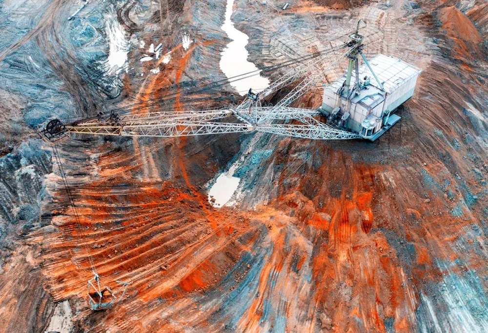 Aerial photograph of a dragline excavator working an iron-ore open-pit mine — the feedstock for Helios's terrestrial low-carbon green-iron process, now its primary near-term business.