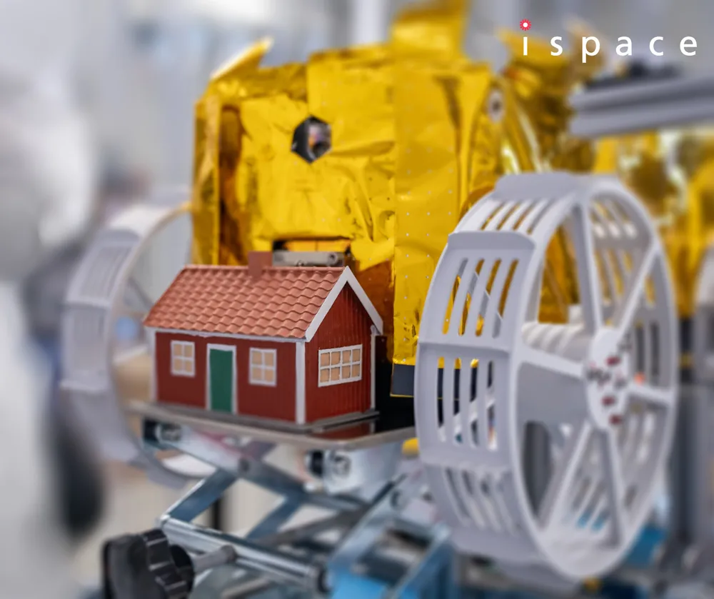 Close-up of the 'Moonhouse' artwork mounted between the wheels of ispace's TENACIOUS micro rover during HAKUTO-R Mission 2 preparation.