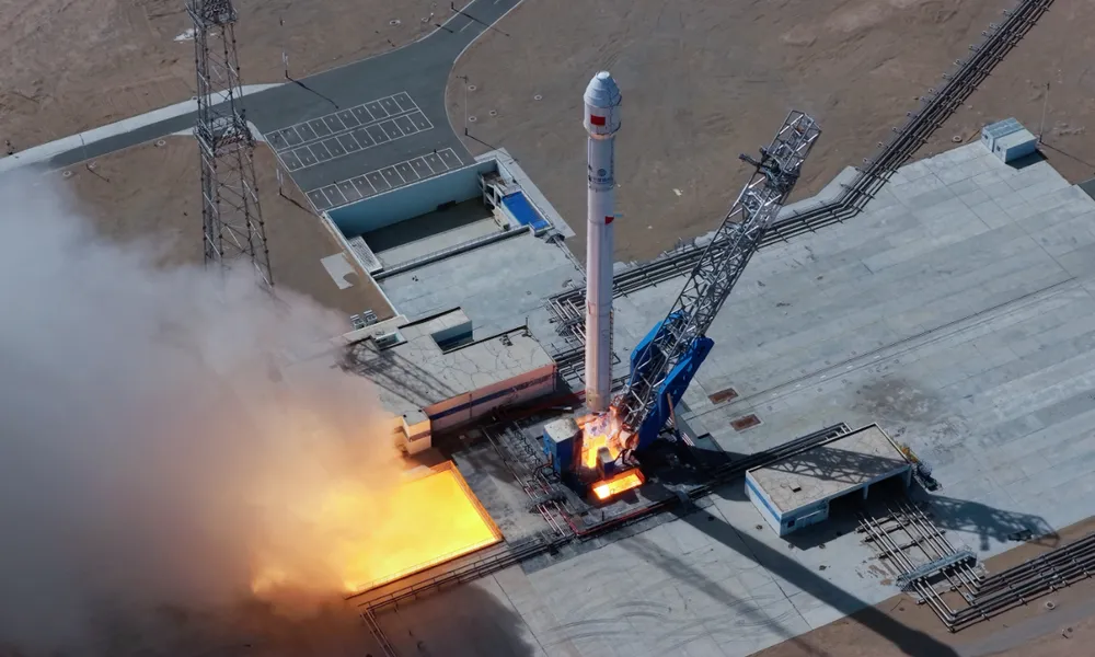 Overhead view of LandSpace's Zhuque-2E methalox rocket lifting off from the Dongfeng pad on 9 June 2026, exhaust glowing in the flame trench beside the erector tower.
