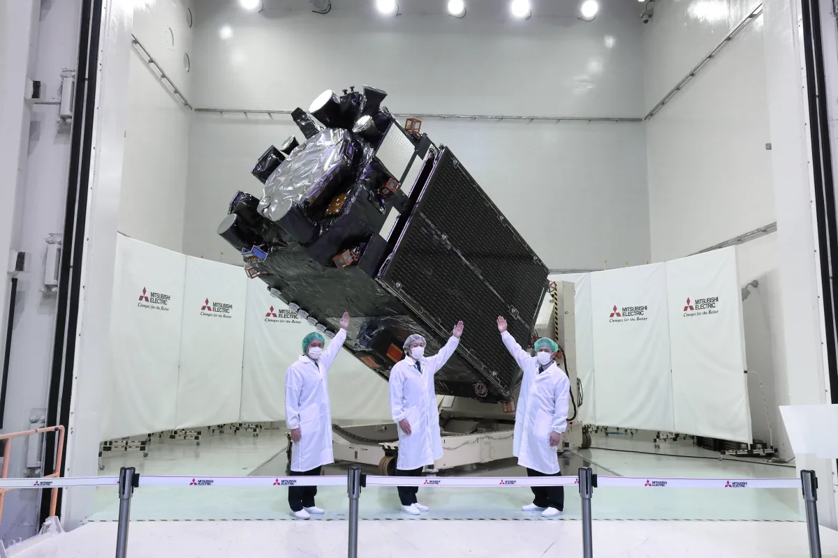 The QZS-6 'Michibiki' navigation satellite — built by Mitsubishi Electric on its DS2000 bus — in the cleanroom, flanked by Mitsubishi Electric panels.