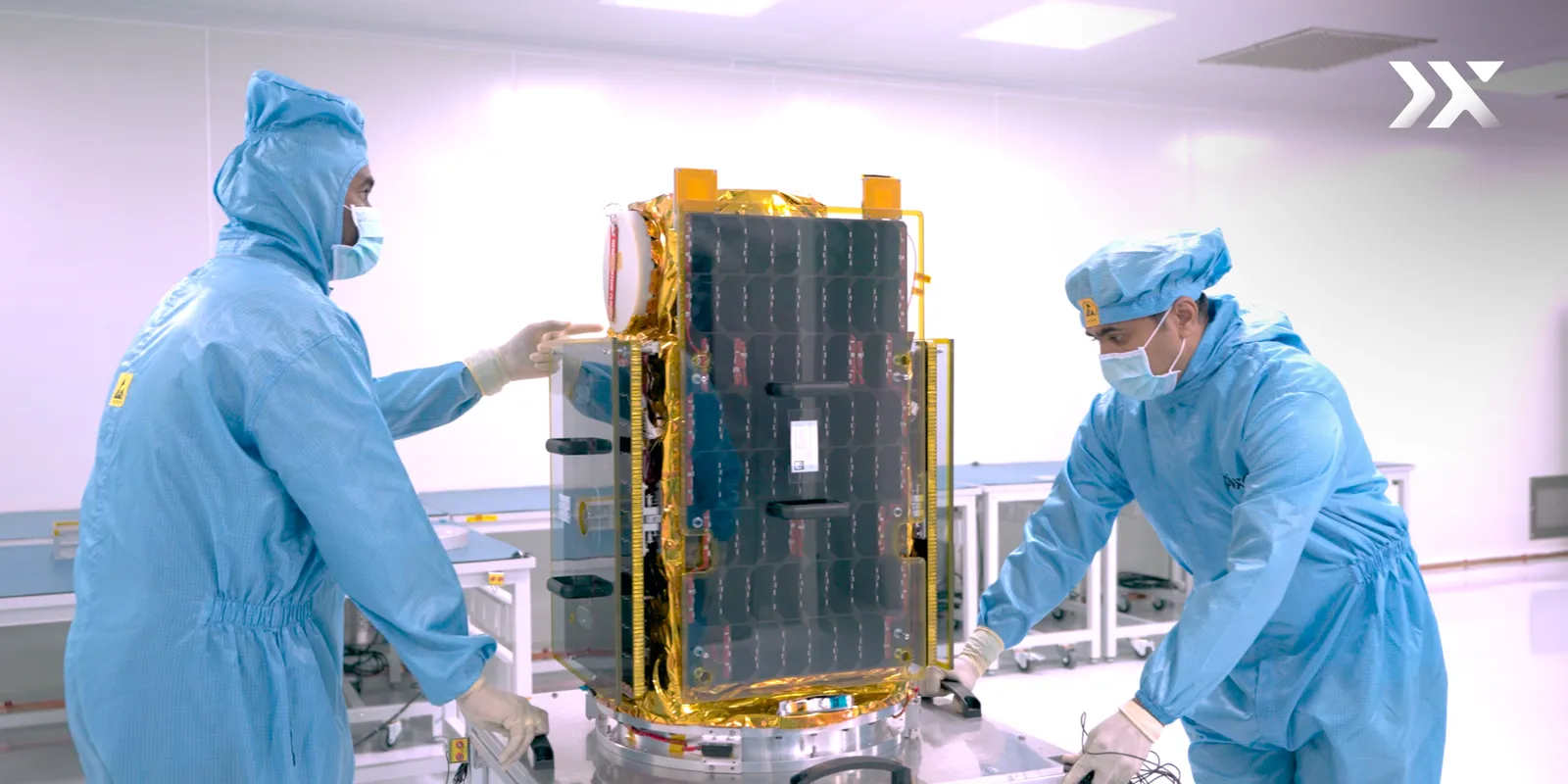 Two Pixxel engineers in cleanroom suits integrate a Firefly hyperspectral satellite, its gold thermal hardware and solar panels visible.