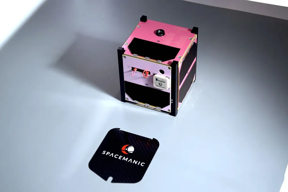 The pink Veronika 1U CubeSat flight unit built by Spacemanic, beside a SPACEMANIC plaque.