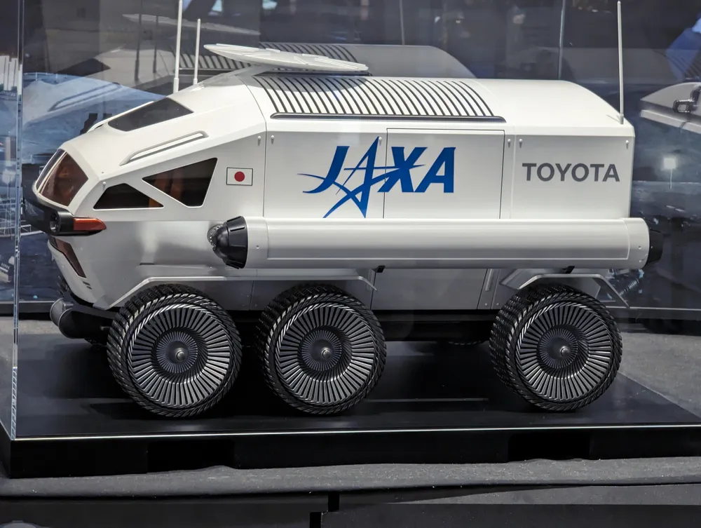 Side-profile view of the Toyota–JAXA pressurised lunar rover model at JAXA's Tsukuba Space Center exhibition hall.