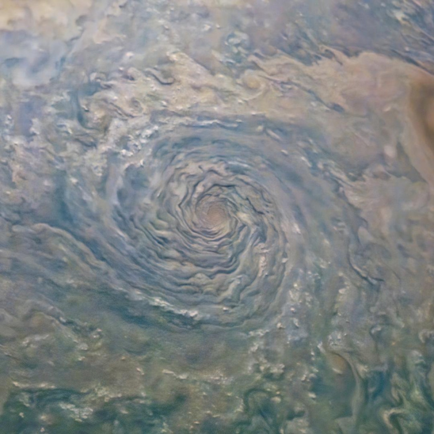 A vast spiral storm in Jupiter's cloud tops, pale blue and cream bands curling into a central eye, imaged by Juno.
