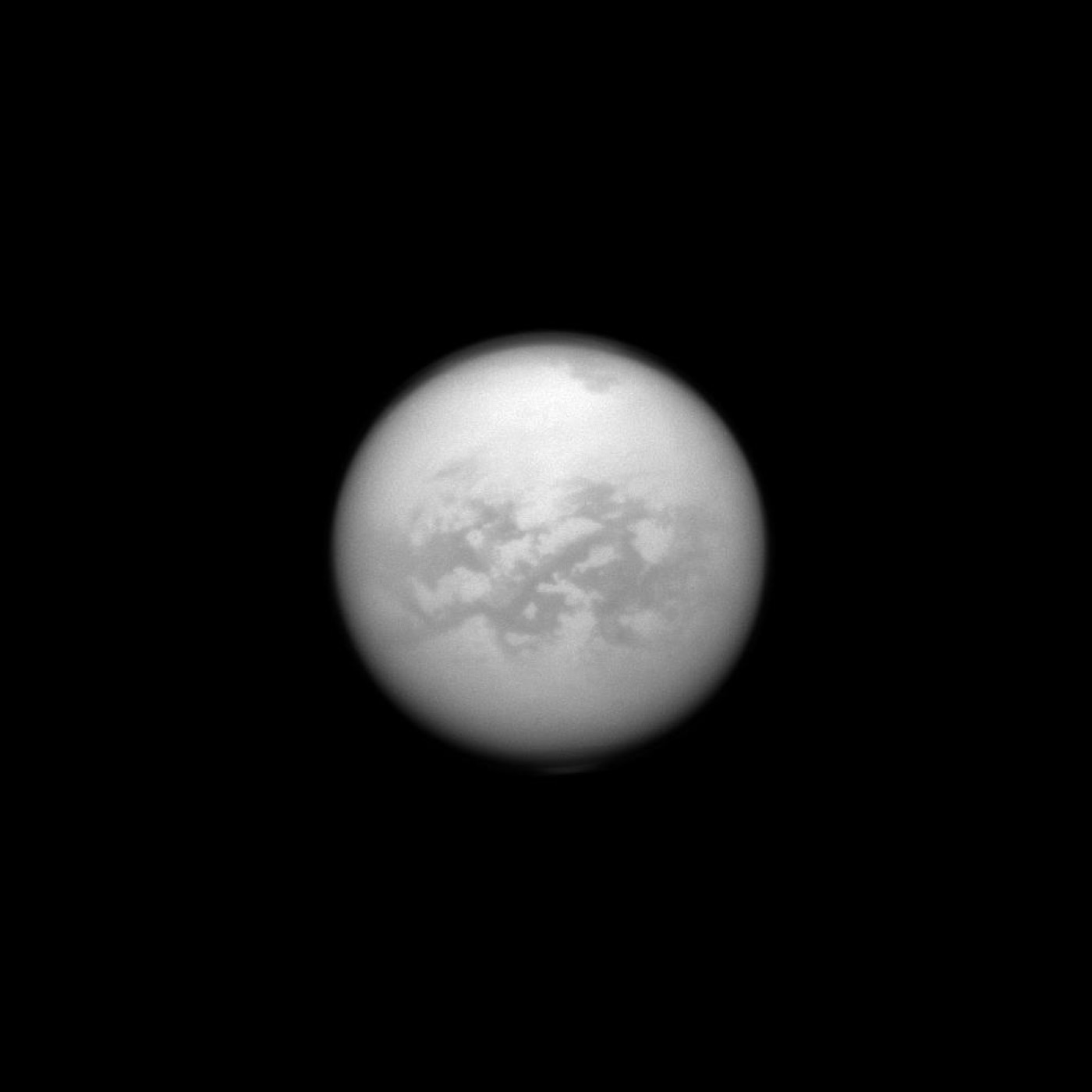Titan seen through its thick orange haze, surface markings barely resolved beneath the atmosphere.