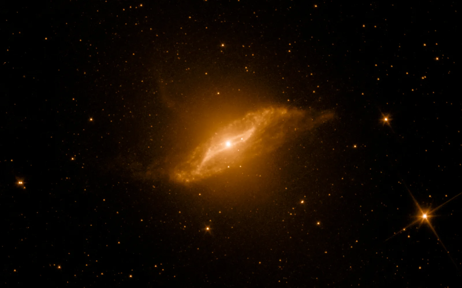 Centaurus A in infrared — Spitzer's infrared view cuts through the dust to reveal a warped, parallelogram-shaped disk at Cen A's heart — the shredded remains of a spiral galaxy it is still digesting.